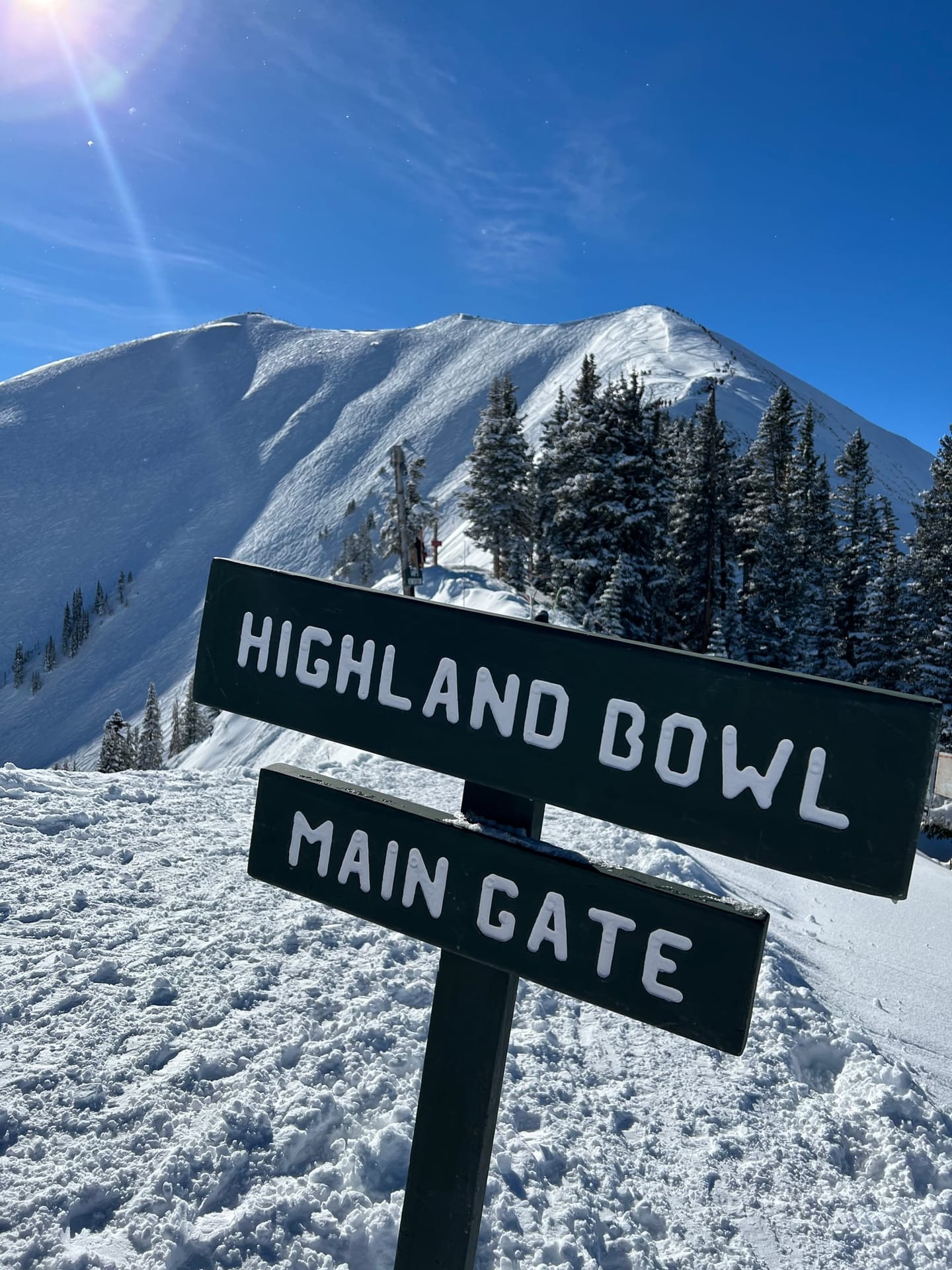 The Highland Bowl Main Gate sign below the snowy ridge of Highland Bowl