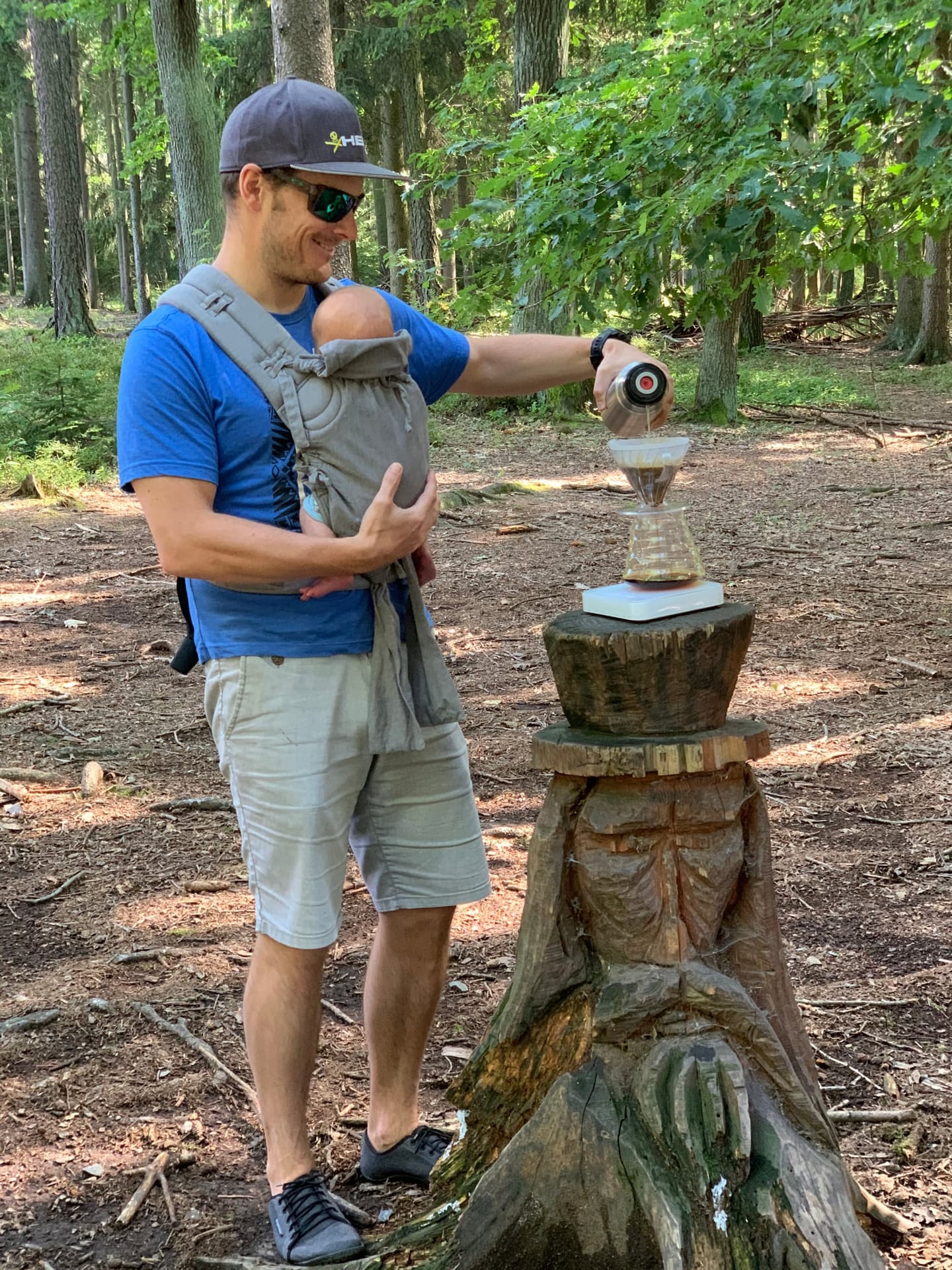 Tomas Mical brewing pour-over coffee in the forest with his baby in a carrier